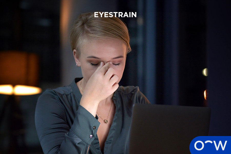 A woman pictured reading from her laptop in the dark, pinching her upper nose while closing her eyes