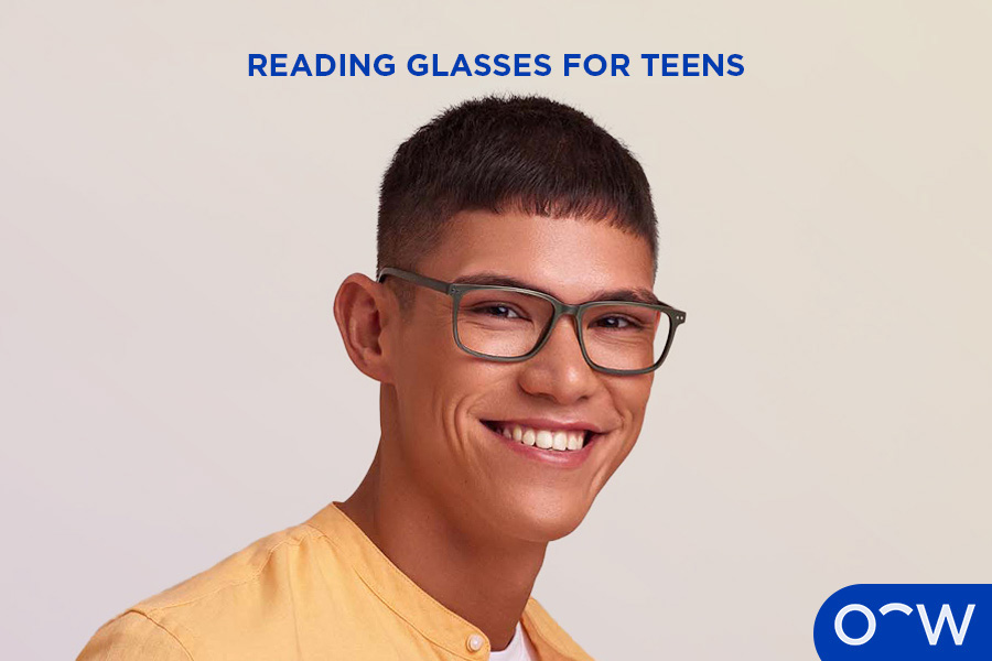 A young man smiling wearing a pair of reading glasses.